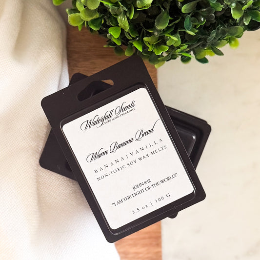 Warm Banana Bread wax melts in a black clamshell container. Non-toxic, hand poured melts with cozy notes of fresh banana, vanilla, and sweet spice.