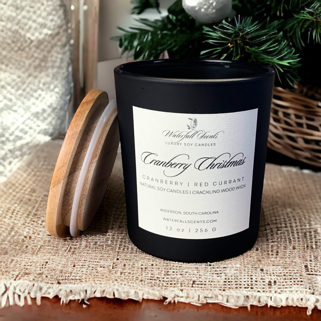 cranberry christmas wooden wick candle in a black matte glass jar on a table with a burlap placemat
