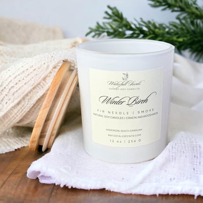 winter birch wooden wick candle in a matte white glass jar on a table with a white cloth